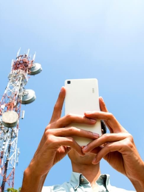 So viel verdienen Praktikanten in der Telekommunikation Mann mit Smartphone vor einem Telefonmast